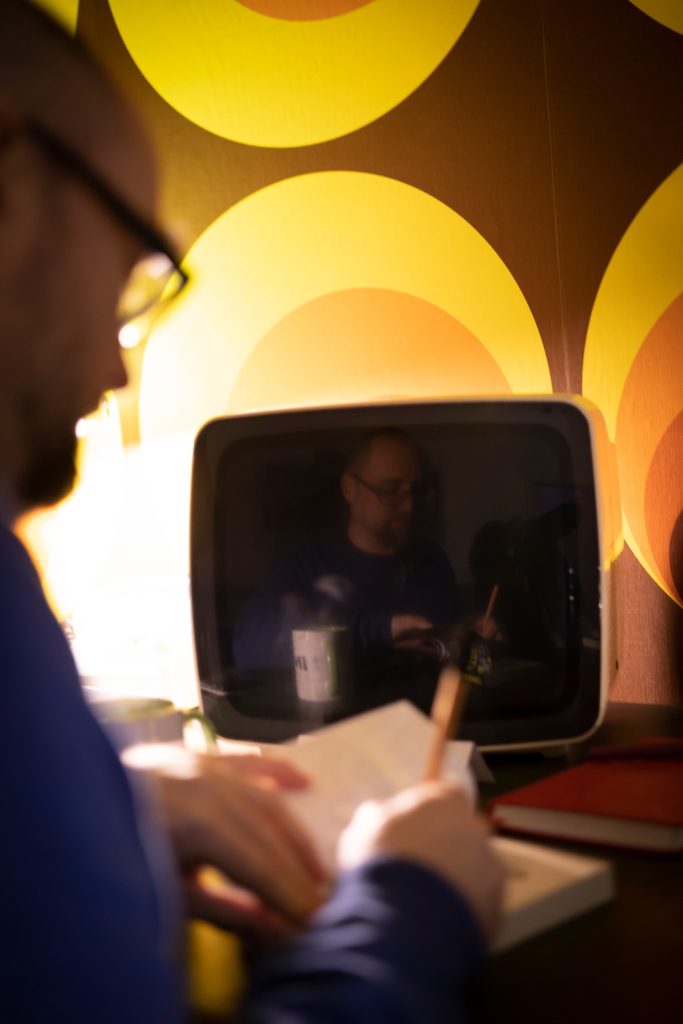 Fabian Mauruschat signiert sein Buch vor einem alten Röhrenfernseher, der ihn spiegelt.